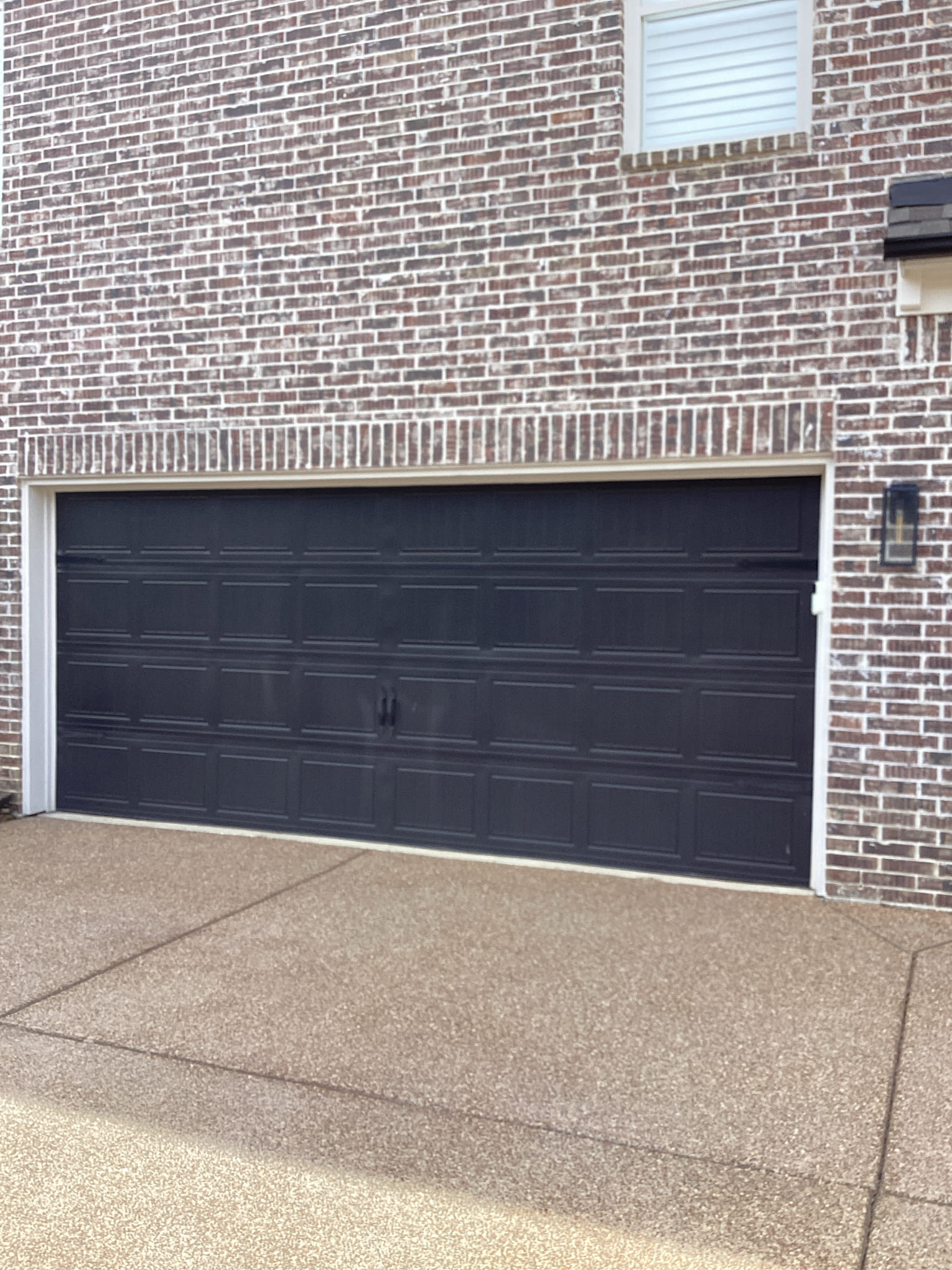 Finished black raised-panel garage door installed on a brick home