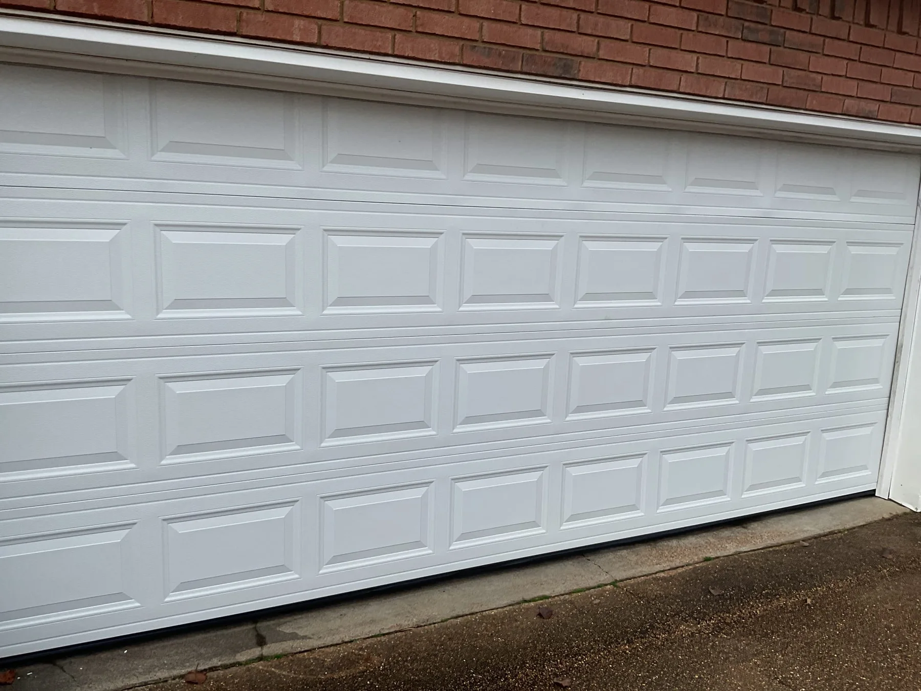 White raised-panel garage door installed by Lift Doctors on a brick home
