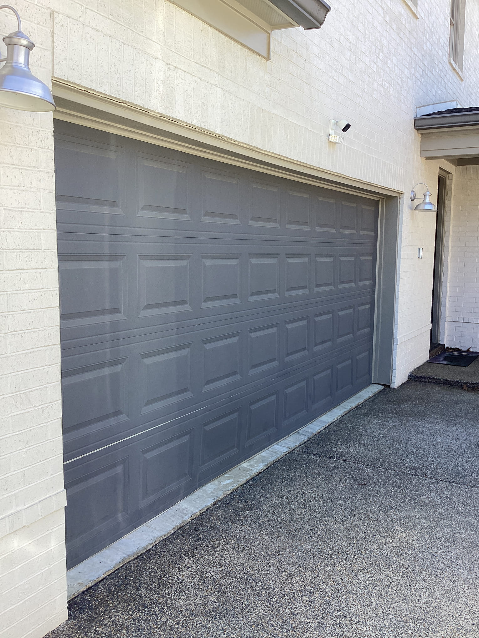 Finished charcoal raised-panel garage door installed on a white brick home