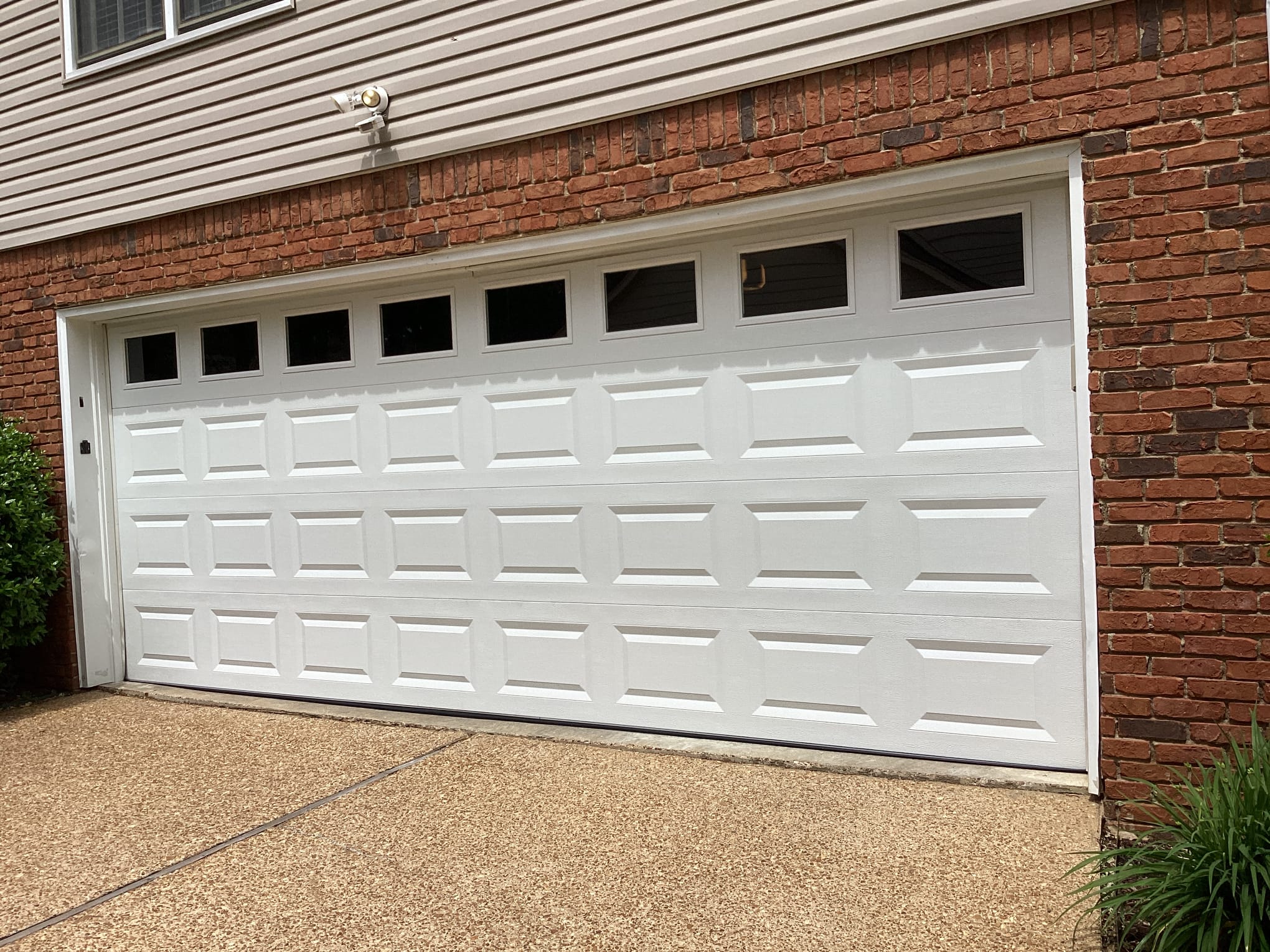Finished white windowed garage door installed on a brick home