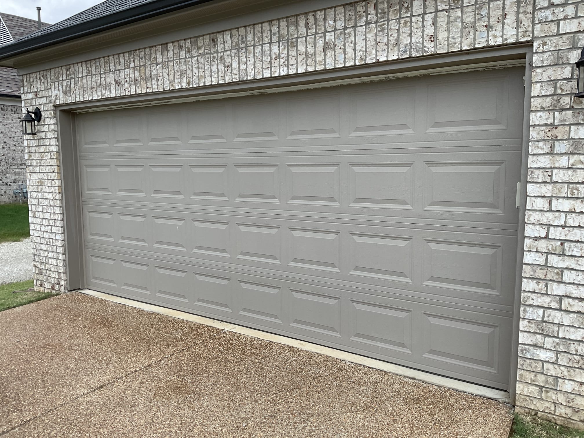 Finished gray raised-panel garage door installed on a brick home