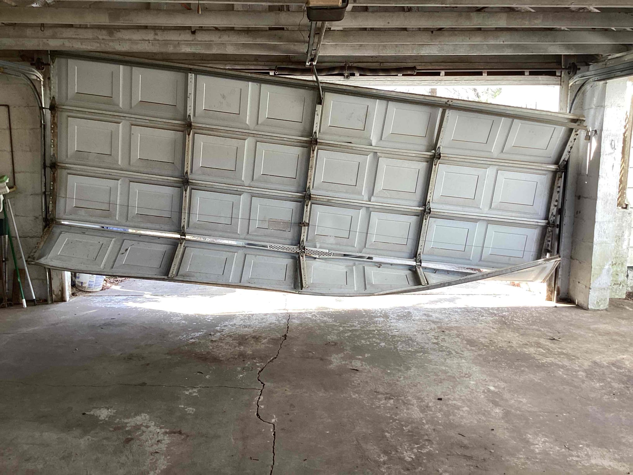Bowed bottom section of a damaged garage door needing urgent repair