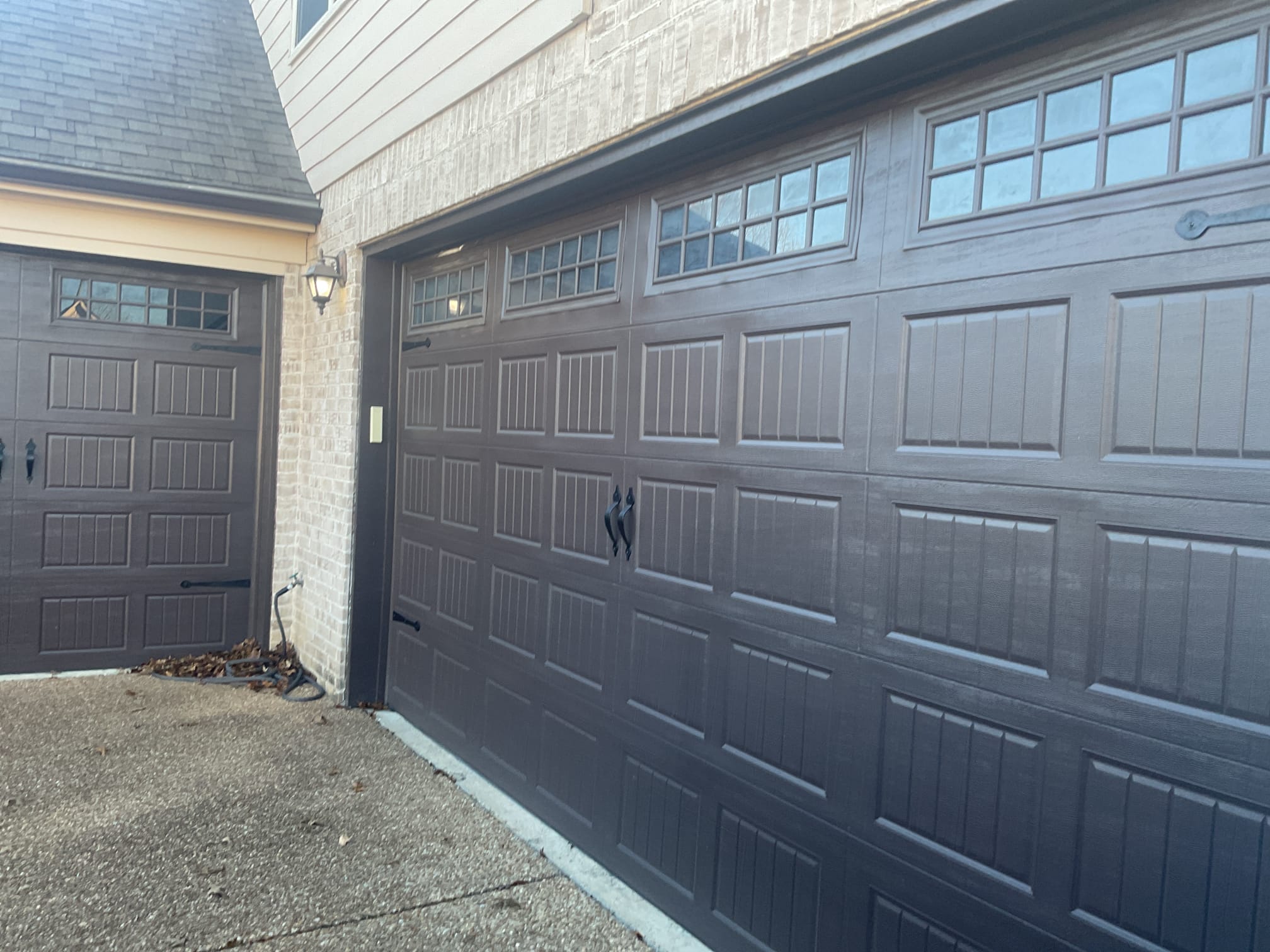 Finished dark carriage-style windowed garage doors on a brick home